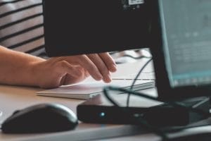 Close-up of a person's hand using a computer mouse, with a blurred computer screen in the background, indicating a work or installation process.